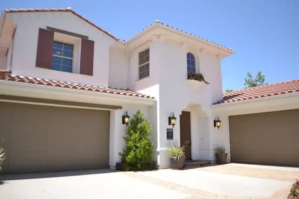 A white house with two garage doors and a tree.